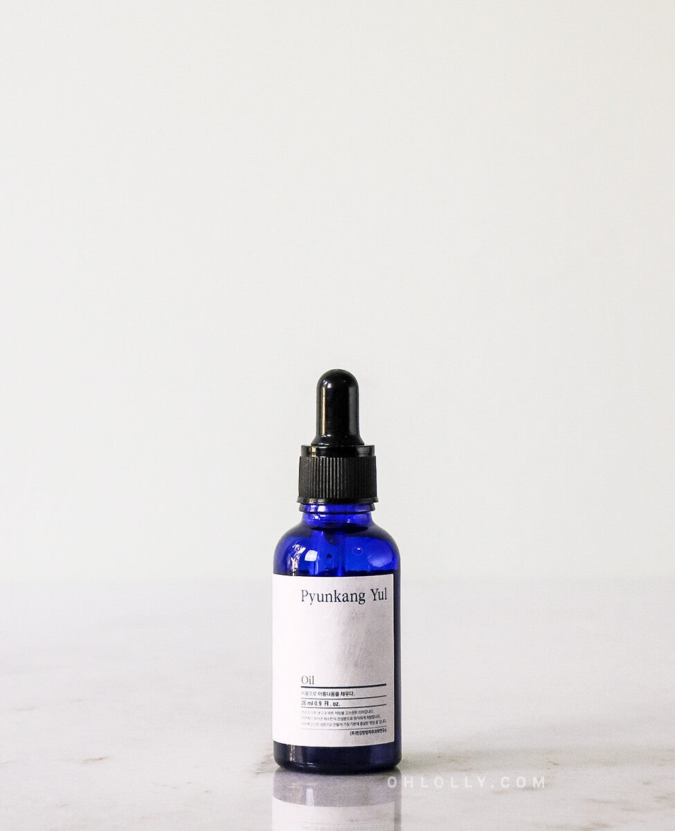 Straight-on studio shot of the Pyunkang Yul Oil in its dark blue glass dropper bottle with a black cap, standing on a light surface against a plain white background.