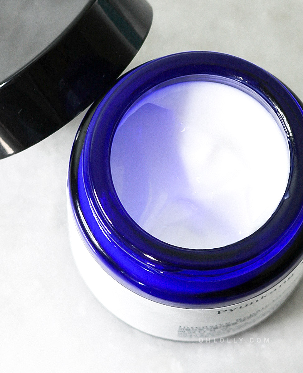 Overhead close-up of the dark blue glass jar of Pyunkang Yul Intensive Repair Cream with the lid off. The rich, white cream is visible, highlighting its thick, deeply moisturizing texture with peptides and shea butter.