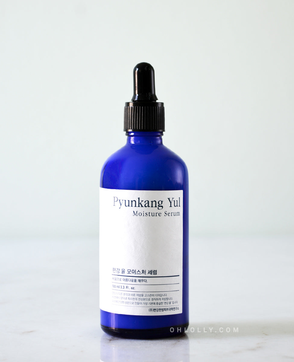 Close up straight-on, detailed shot of the Pyunkang Yul Moisture Serum's dark blue glass bottle, focusing on the white rectangular label and the product name