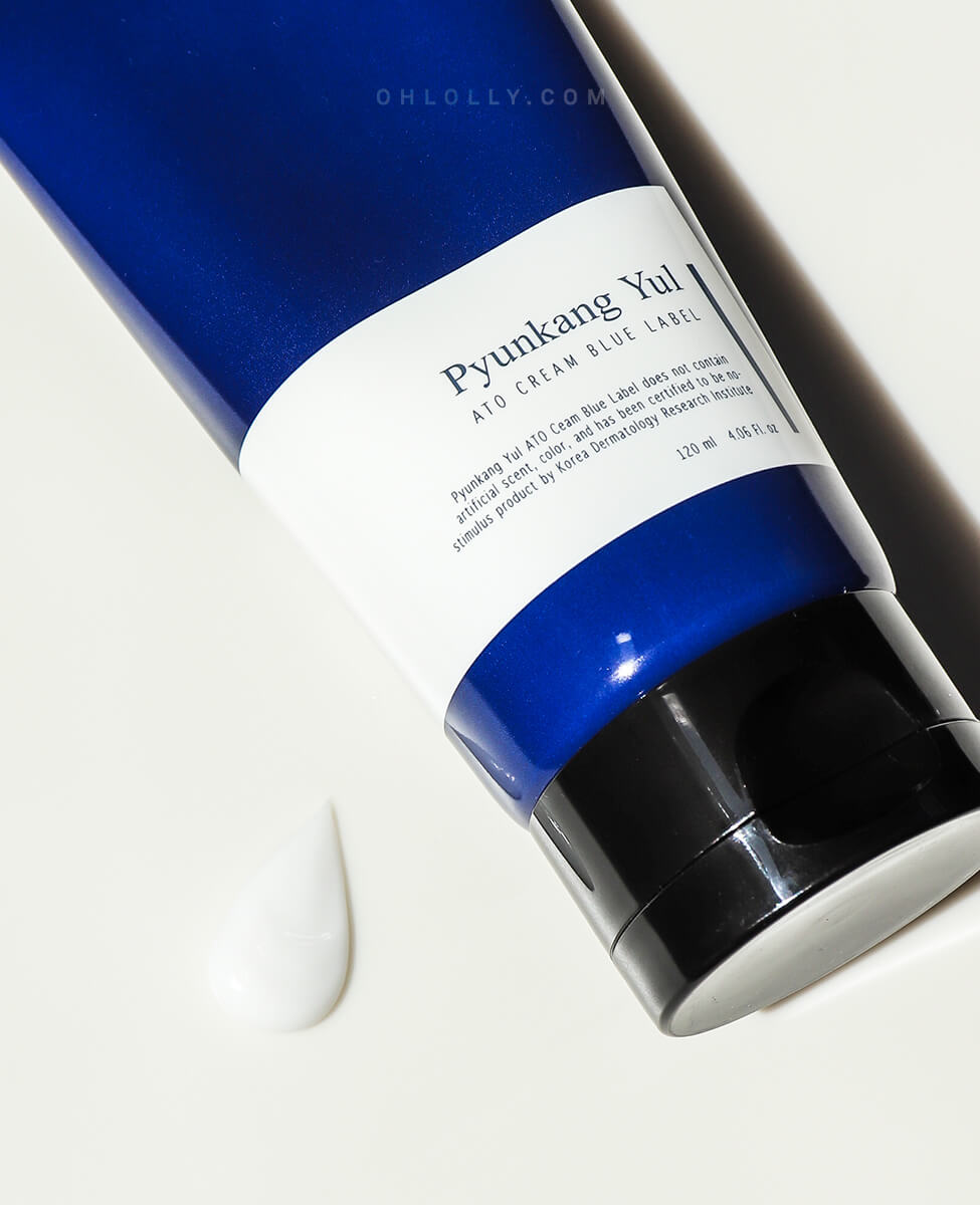 Extreme close-up studio shot of the dark blue Pyunkang Yul ATO Cream Blue Label tube, focusing on the white label text and the black cap. A dollop of the rich, white cream is visible, highlighting the product's nourishing texture with ceramides and peptides.