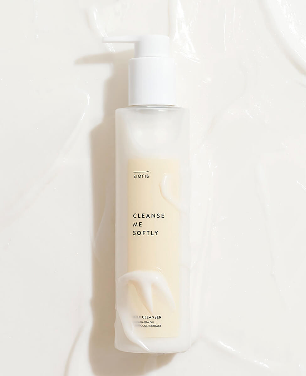 Sioris Cleanse Me Softly Milk Cleanser bottle with organic green plum water on white background with product all around showing its texture