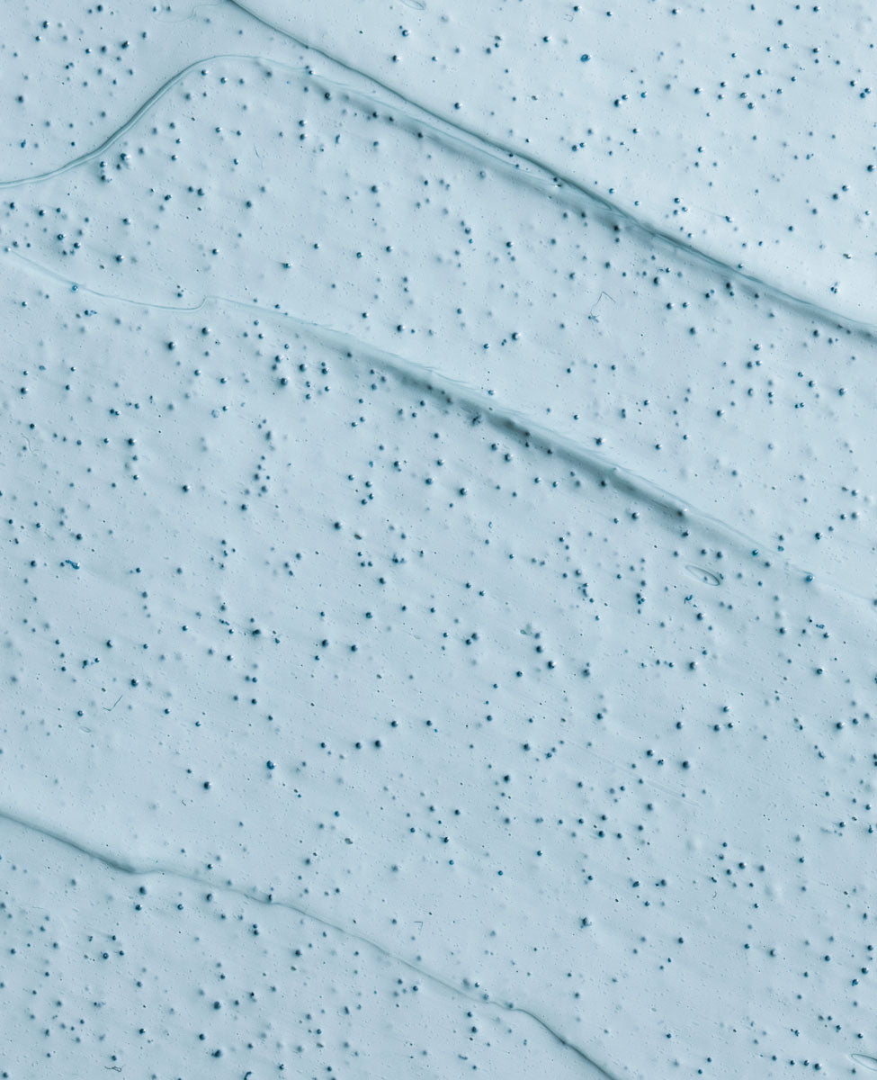 Extreme close-up of the Urang Clarifying Blue Mask texture, clearly showing the creamy blue clay and tiny jojoba beads for gentle, non-irritating exfoliation.