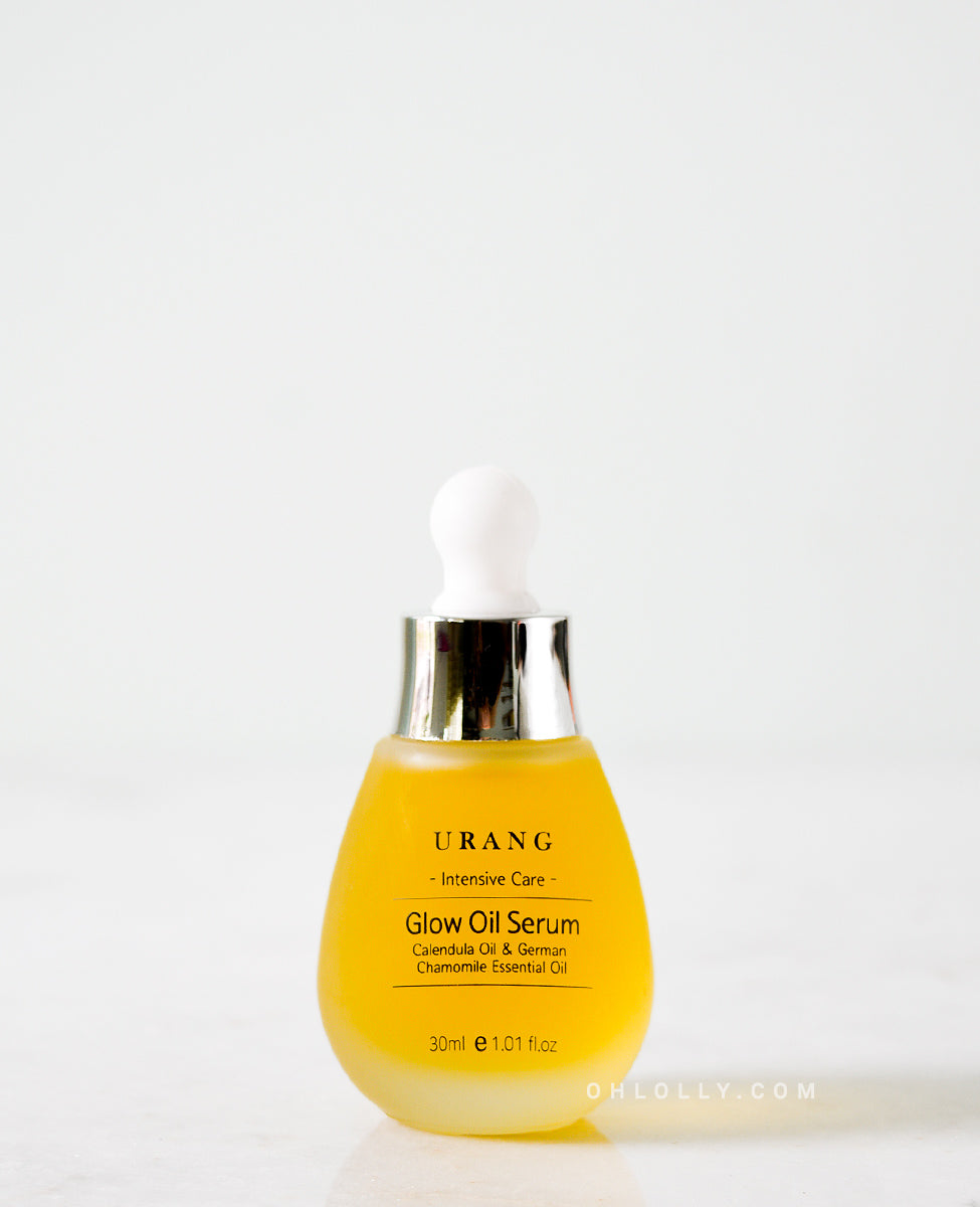 Close-up of the Urang Glow Oil Serum in a frosted glass dropper bottle with a white and silver cap, showing the bright yellow oil inside.