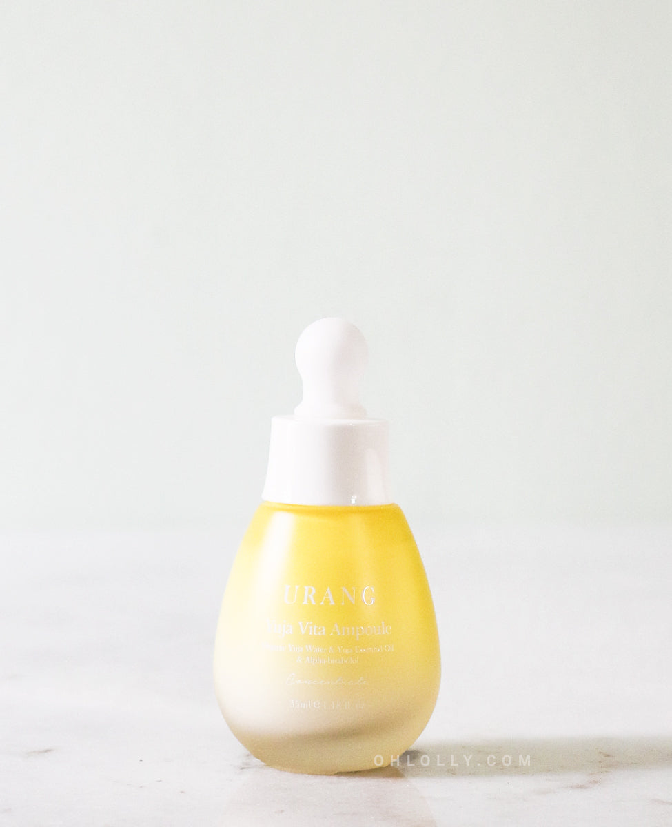 The Urang Yuja Vita Ampoule in a small, frosted glass dropper bottle with a white and gold cap, showcasing the milky, pale yellow ampoule inside on a white surface.