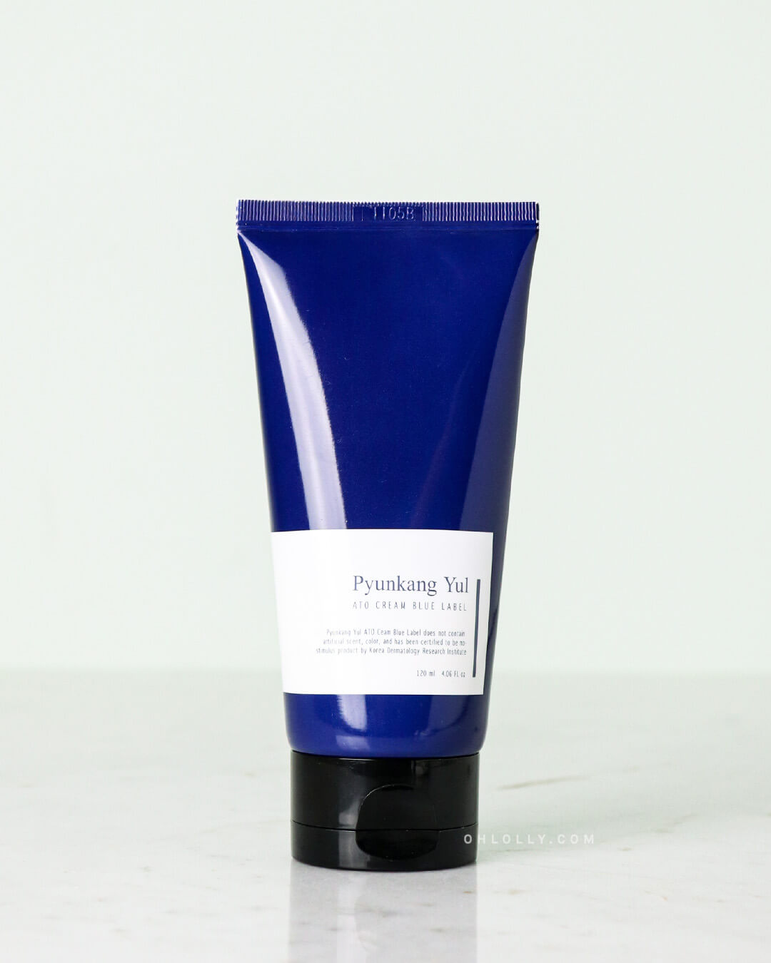 Front-on product shot of the dark blue Pyunkang Yul ATO Cream Blue Label tube, highlighting the white label with 'Pyunkang Yul ATO Cream' text. The tube stands upright on a pale marble surface, emphasizing its simple, clean packaging.