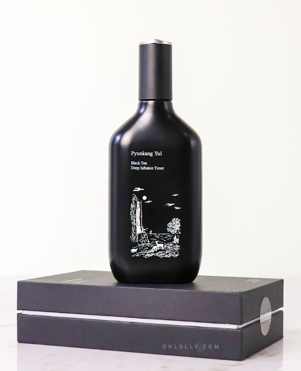 Front-on studio shot of the black Pyunkang Yul Black Tea Deep Infusion Toner bottle standing on its black, matte outer box. The bottle features a distinct white illustration of a waterfall, emphasizing the product's premium, anti-aging, and deeply nourishing formula.