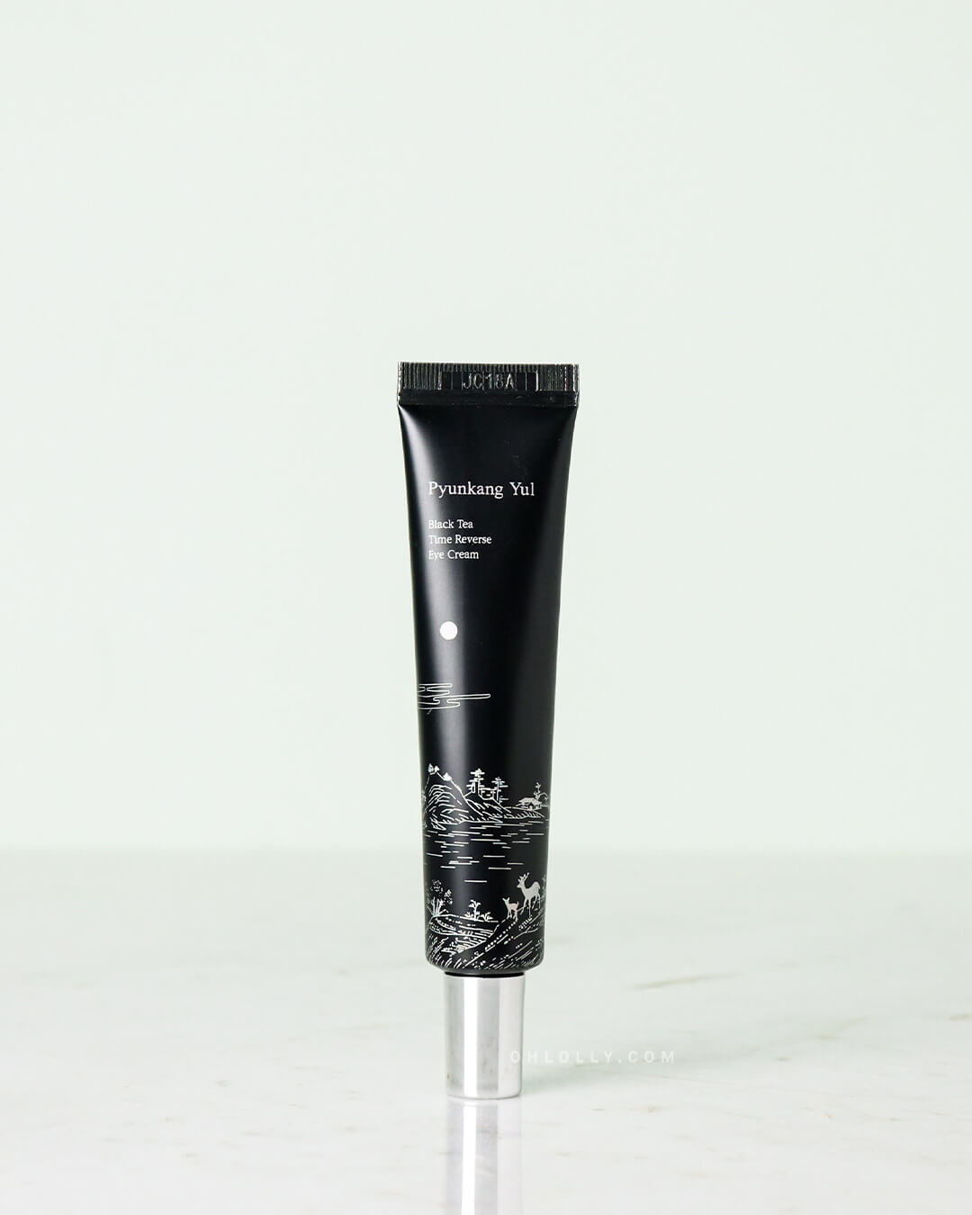 Front-on studio shot of the black Pyunkang Yul Black Tea Time Reverse Eye Cream tube standing upright. The white product label and an elegant illustration of a deer and landscape are visible, highlighting the product's focus on anti-aging and firming.