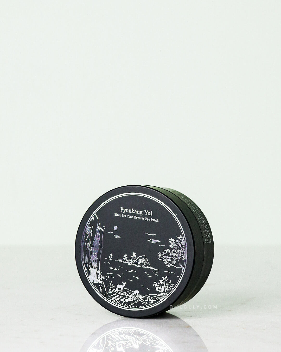Front-on studio shot of the black Pyunkang Yul Black Tea Time Reverse Eye Patch jar. The jar features an elegant white illustration of a deer and landscape, emphasizing the patches' anti-aging benefits with black tea and hydrogel material.
