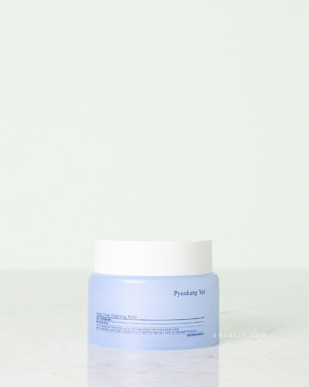 Front-on studio shot of the Pyunkang Yul Deep Clear Cleansing Balm jar. The short, light blue jar with a white lid is centered on a pale surface, highlighting the balm-to-oil first cleanser for barrier-boosting hydration.