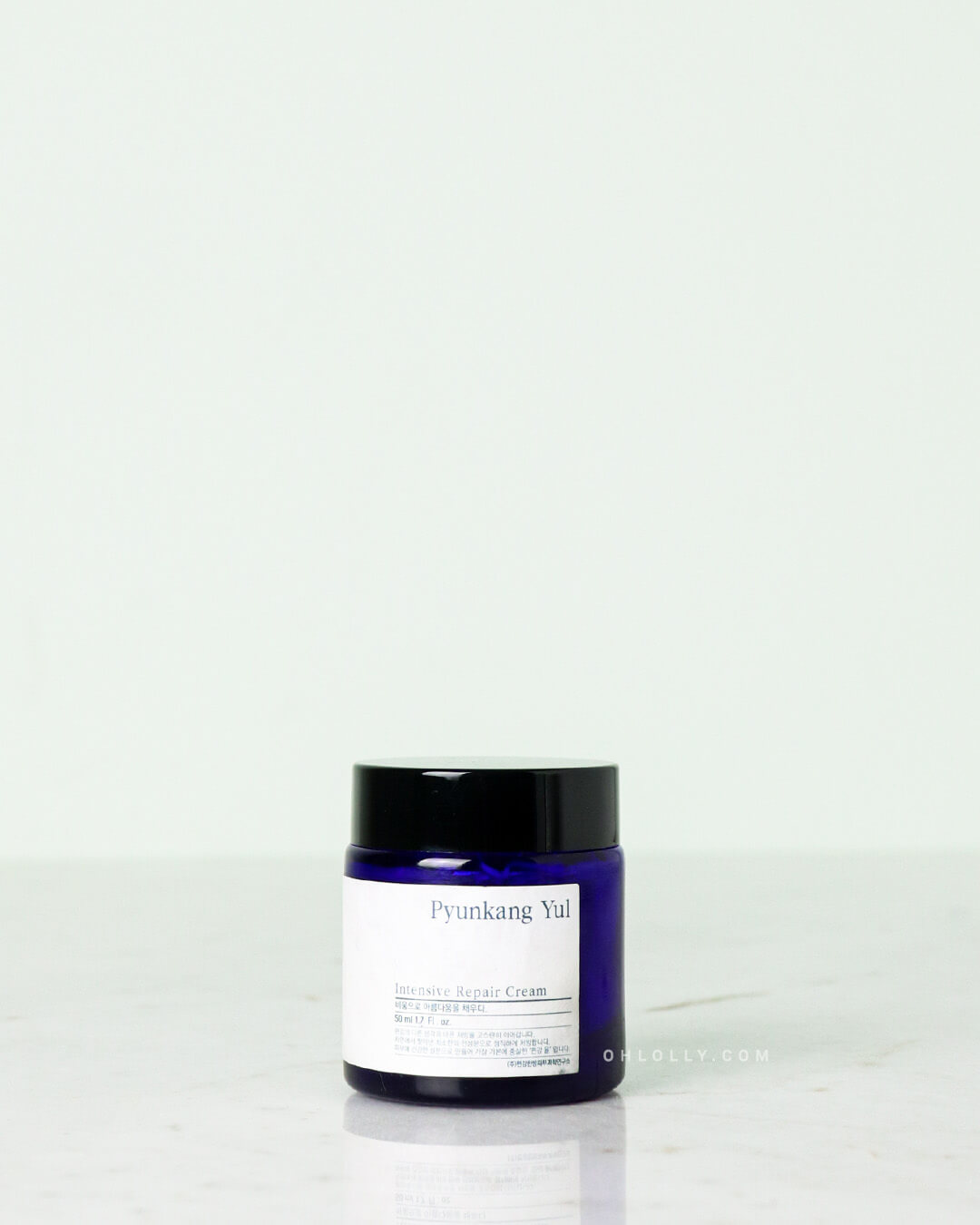 Studio shot of the Pyunkang Yul Intensive Repair Cream. The rich, blue glass jar with a black lid is centered on a white marble surface, clearly displaying the white rectangular label on its side.
