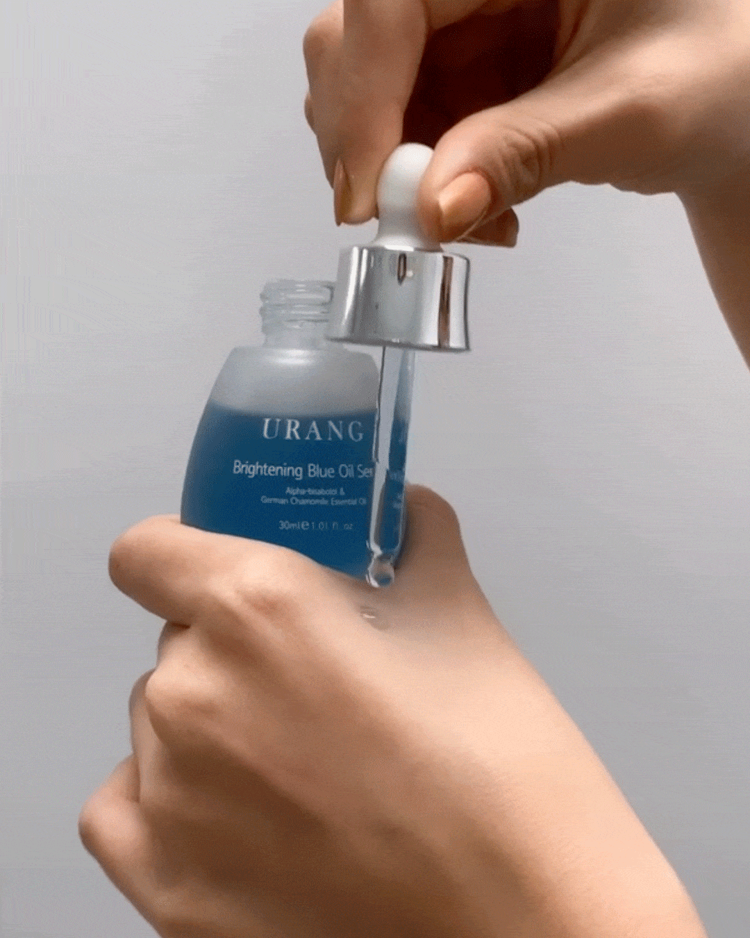 Close-up of a drop of Urang Blue Oil Serum being applied to skin, showing the lightweight texture and quick absorption.