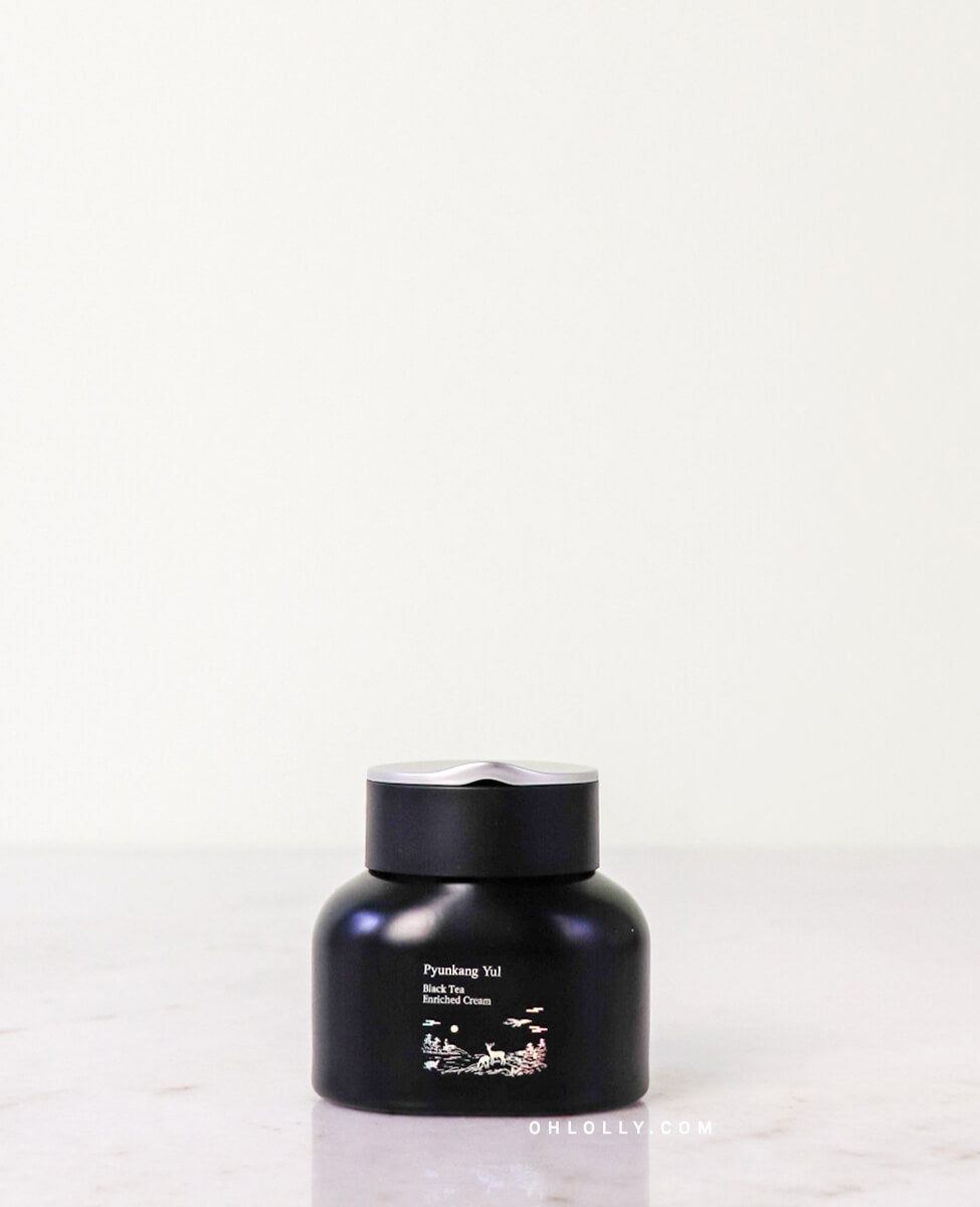 Front-on studio shot of the black Pyunkang Yul Black Tea Enriched Cream jar. The jar features a small white label with an elegant illustration of a deer and landscape, emphasizing the product's rich, anti-aging formula and premium design.