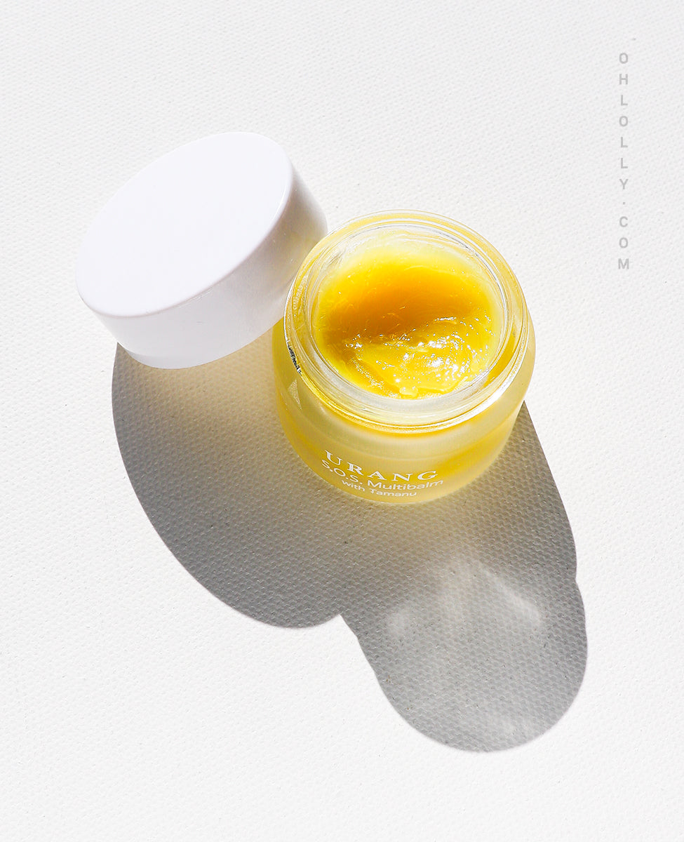 Overhead view of the Urang S.O.S. Multi Balm with Tamanu in a small, clear glass jar, showcasing the solid, yellow balm.