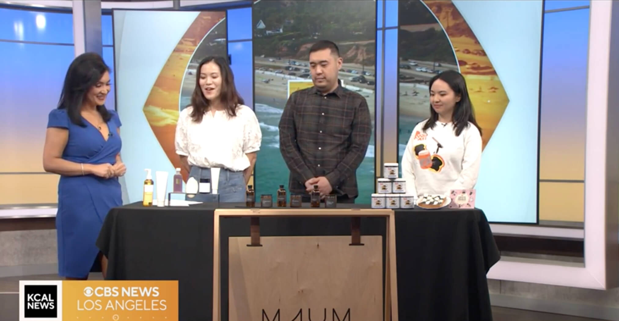  Four people stand behind a table with skincare products during a KCAL News segment with Rachel Kim.