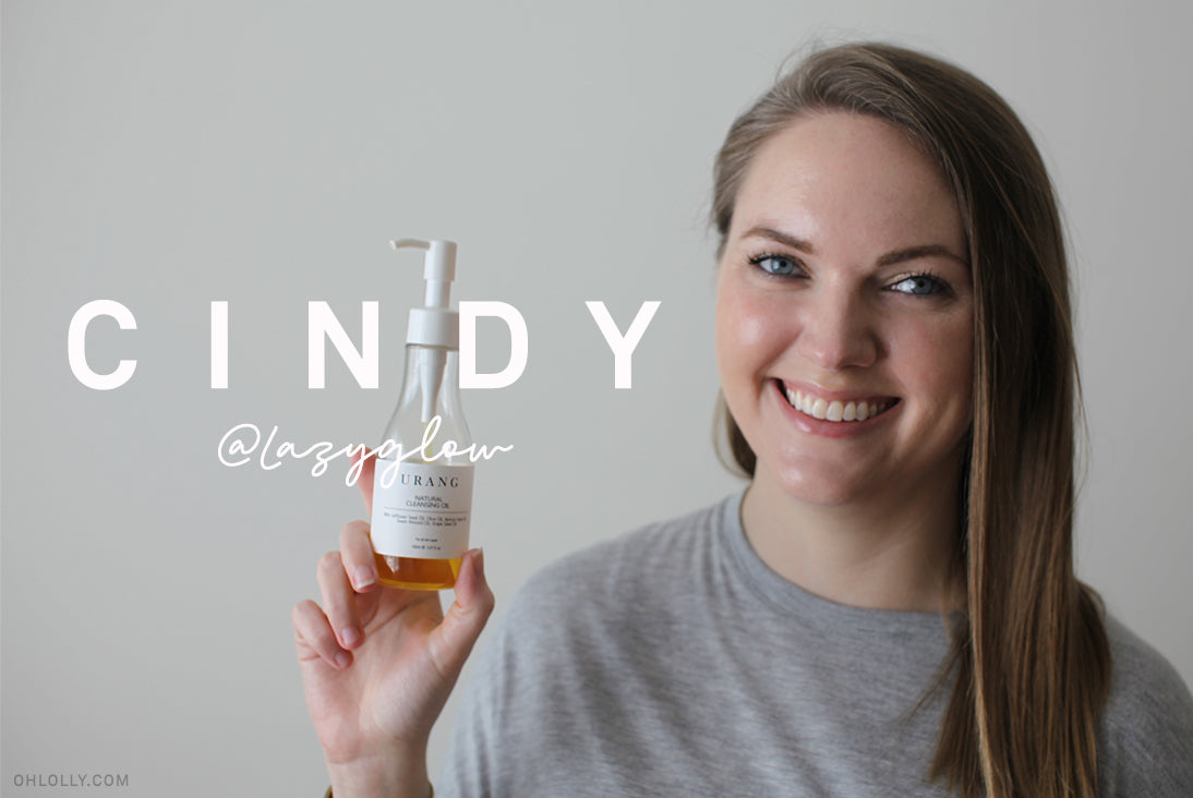 Beauty blogger Cindy (@lazyglow) smiling and holding a bottle of URANG cleansing oil. Skincare review portrait.