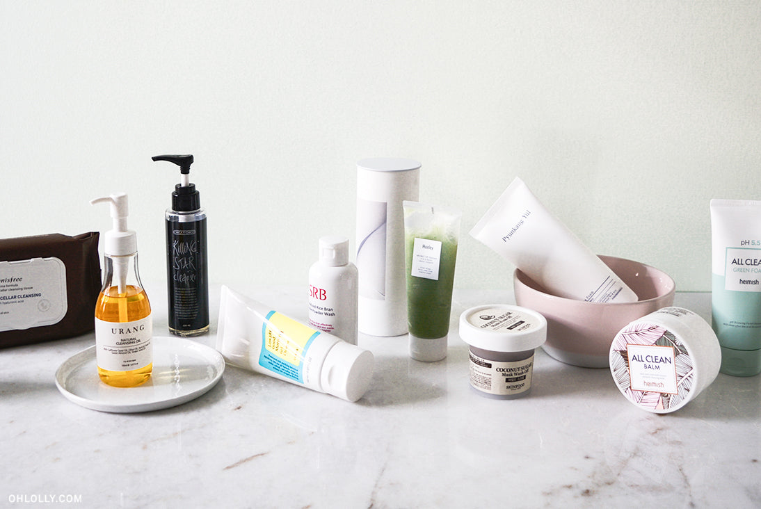 Assorted K-beauty facial cleansers including Urang oil and Huxley water on a marble surface for a complete routine.