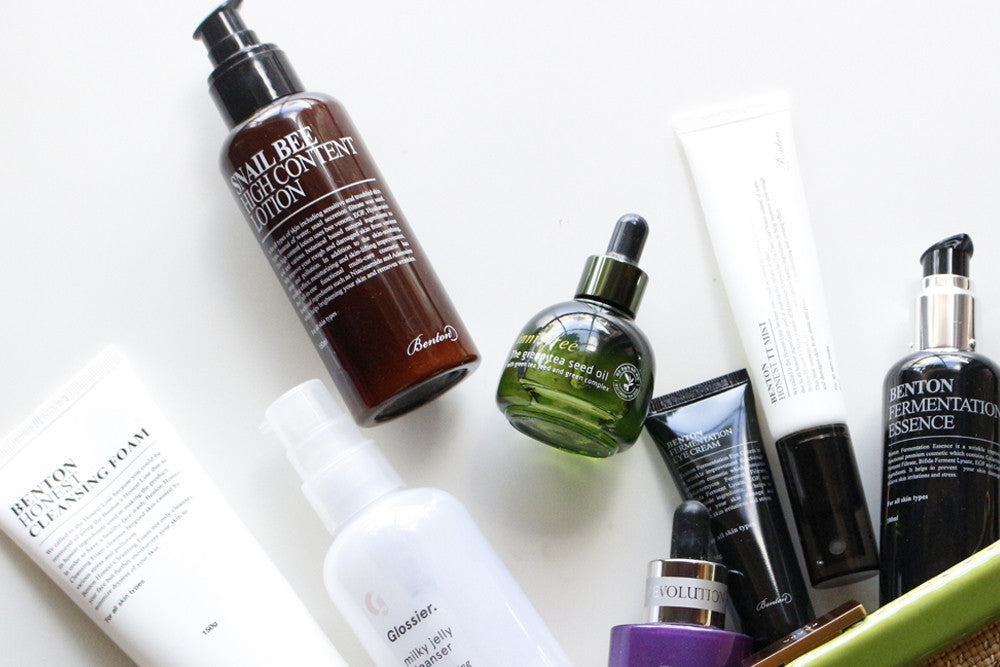 A flat lay of several Korean skincare products, including various bottles and tubes of cleansing foam, essence, and snail bee content, arranged on a white surface.