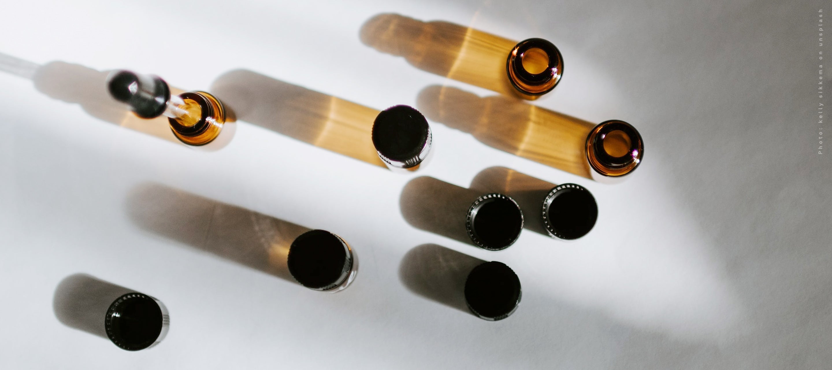  Small amber glass vials and droppers arranged on a white surface, representing essential oils, concentrated extracts, or skincare ingredients for formulation.