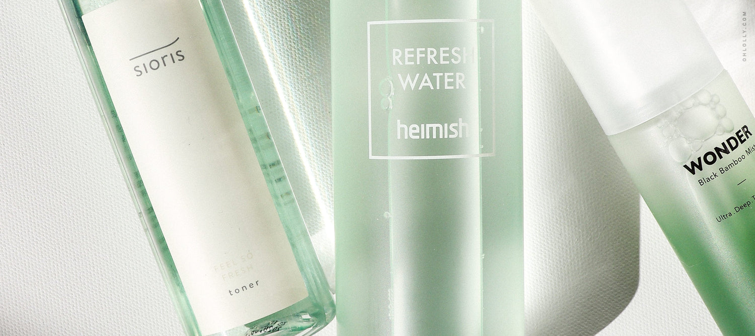 A close-up of three green-tinted skincare bottles from brands including Sioris, Heimish, and Haruharu Wonder, arranged horizontally on a white surface.