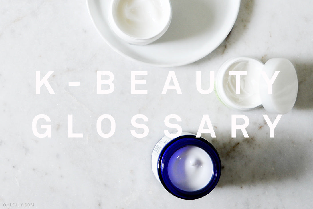 Close-up of various small jars of skincare cream on a white surface, with "K-BEAUTY GLOSSARY" overlaid in large text.