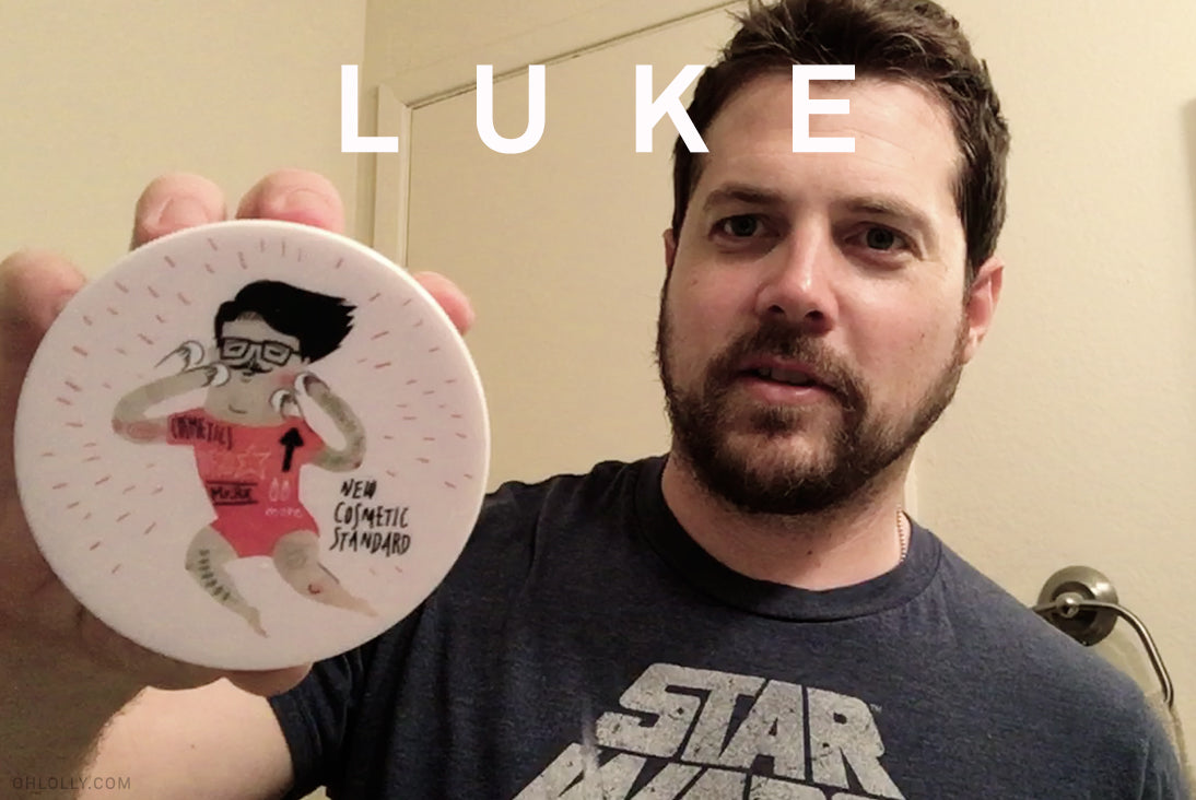  A man with a beard wearing a Star Wars t-shirt holds up a round cosmetic container with an illustrated character and the text "New Cosmetic Standard."