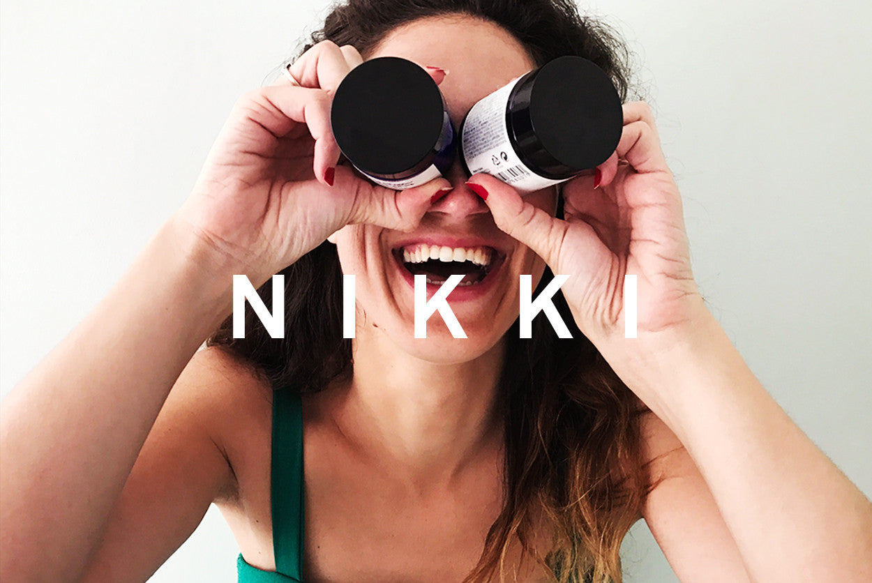 A woman looking through two product jars like binoculars, with the word "NIKKI" overlaid on the image.