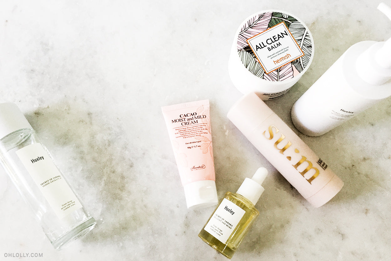  A flat lay of several Korean skincare products including the Heimish All Clean Balm, a Su:m37 cleansing stick, a toner bottle, and serums on a white marble surface.