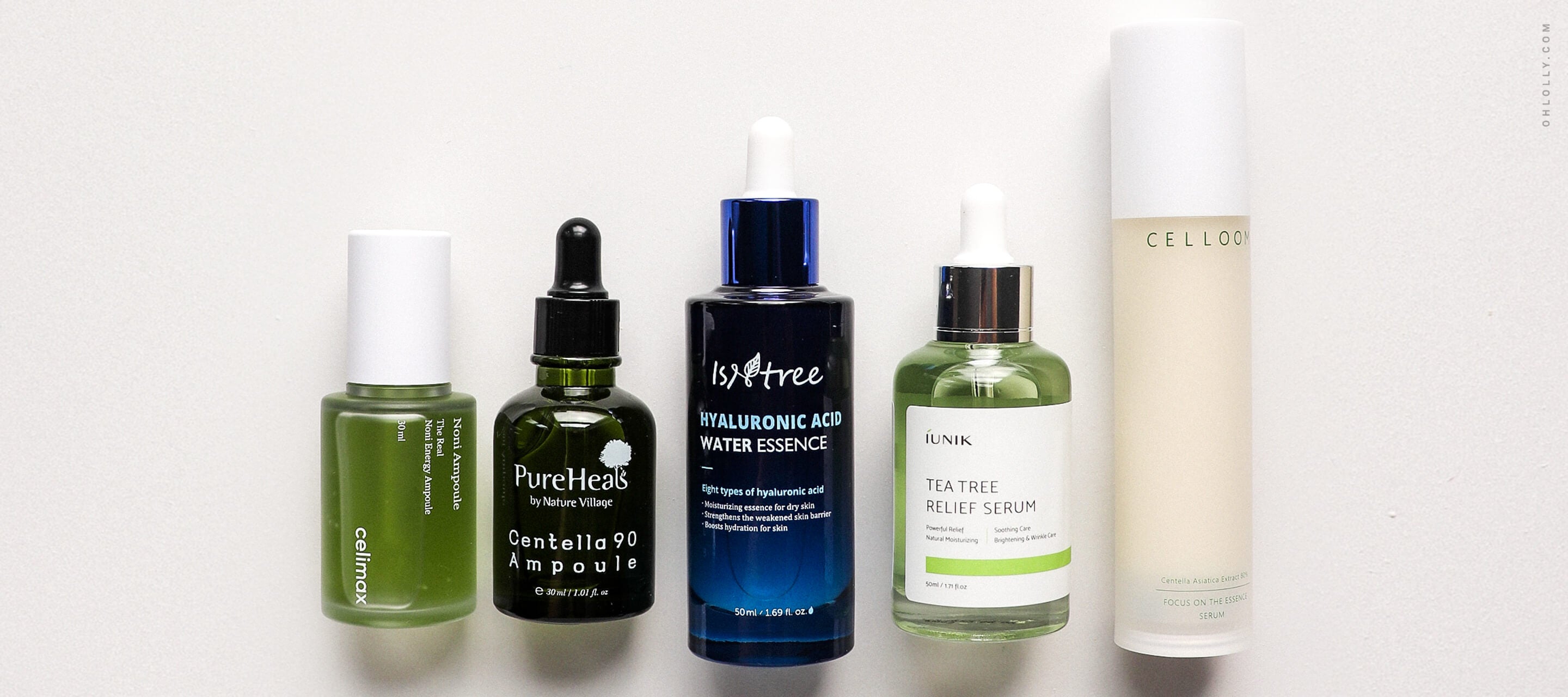 A lineup of five different skincare treatment bottles of various heights and colors, including green, dark blue, and white, arranged against a plain white background.