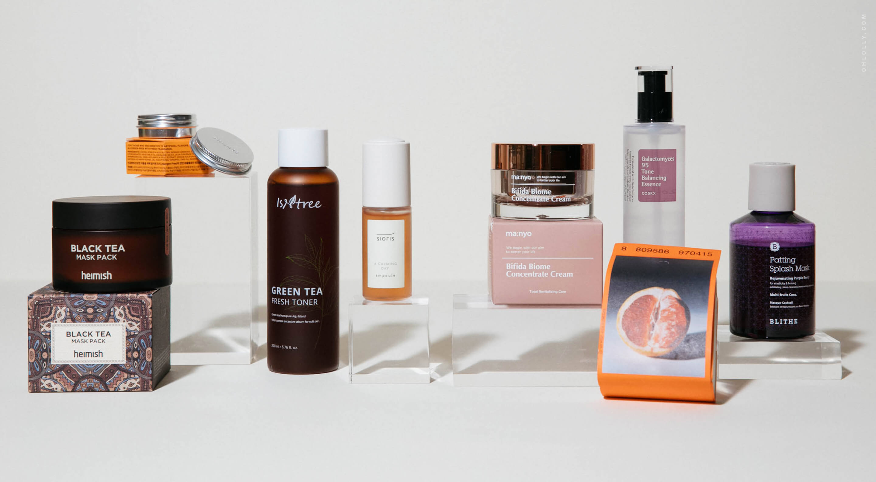  An assortment of various Korean skincare products, including jars, bottles, and serums, arranged neatly on white blocks against a plain light grey background.