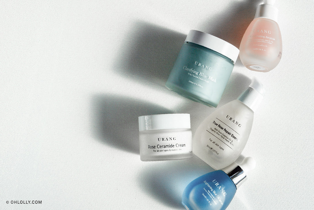 Five URANG skincare products, including various bottles, jars, and a dropper, arranged on a white surface with soft shadows.