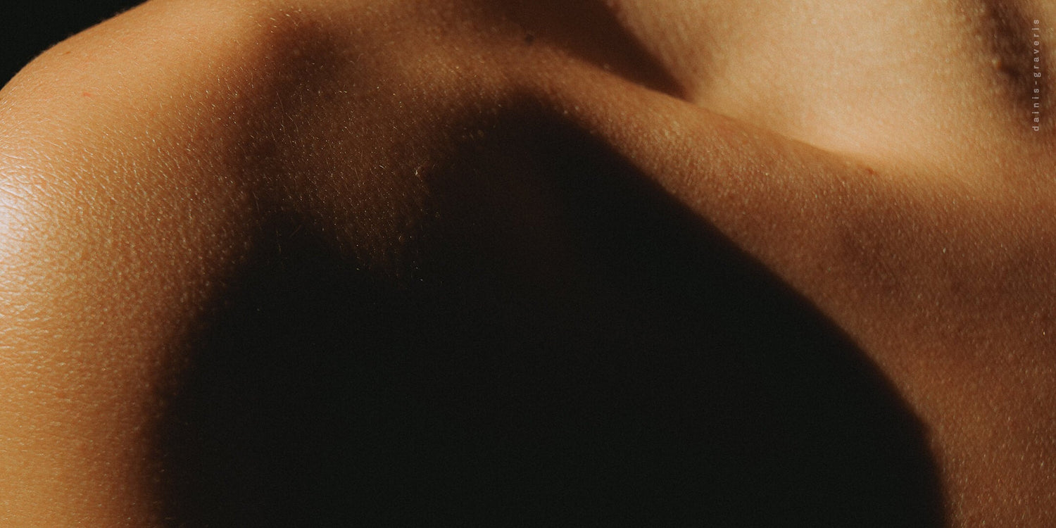  A close-up, artistic shot of a person’s shoulder and collarbone area, highlighted by dramatic light and deep shadows on the skin.