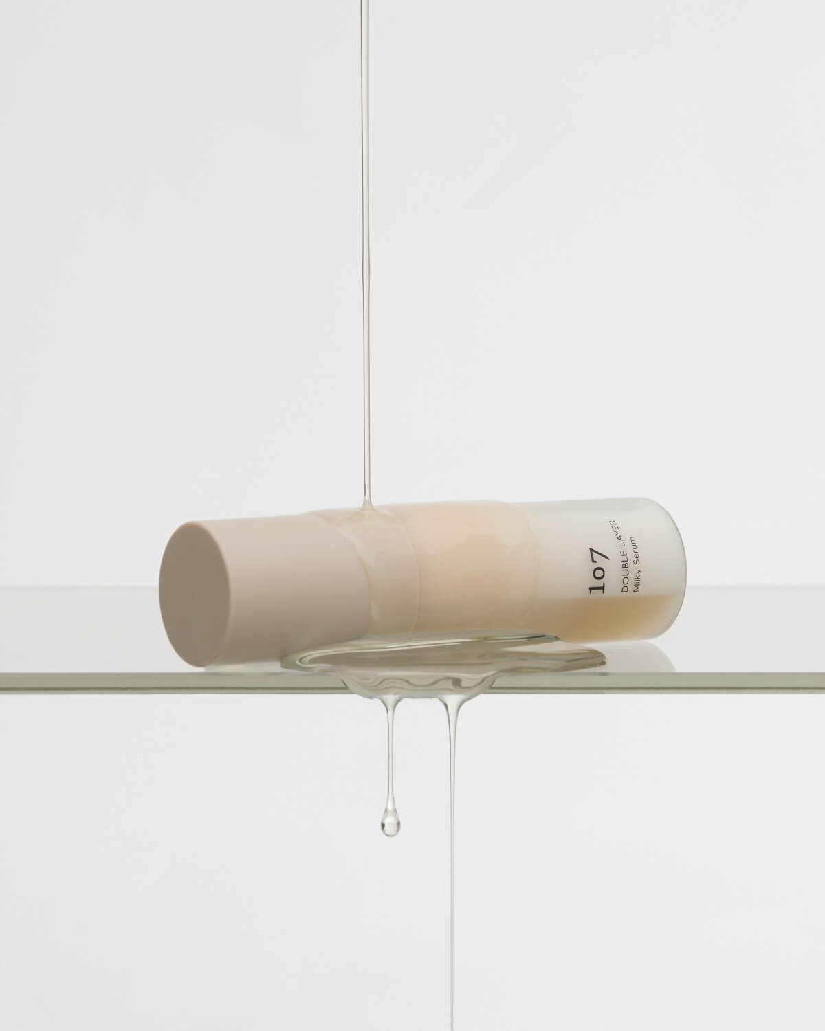 107 Double Layer Milky Serum bottle laying in a pool of clear liquid.