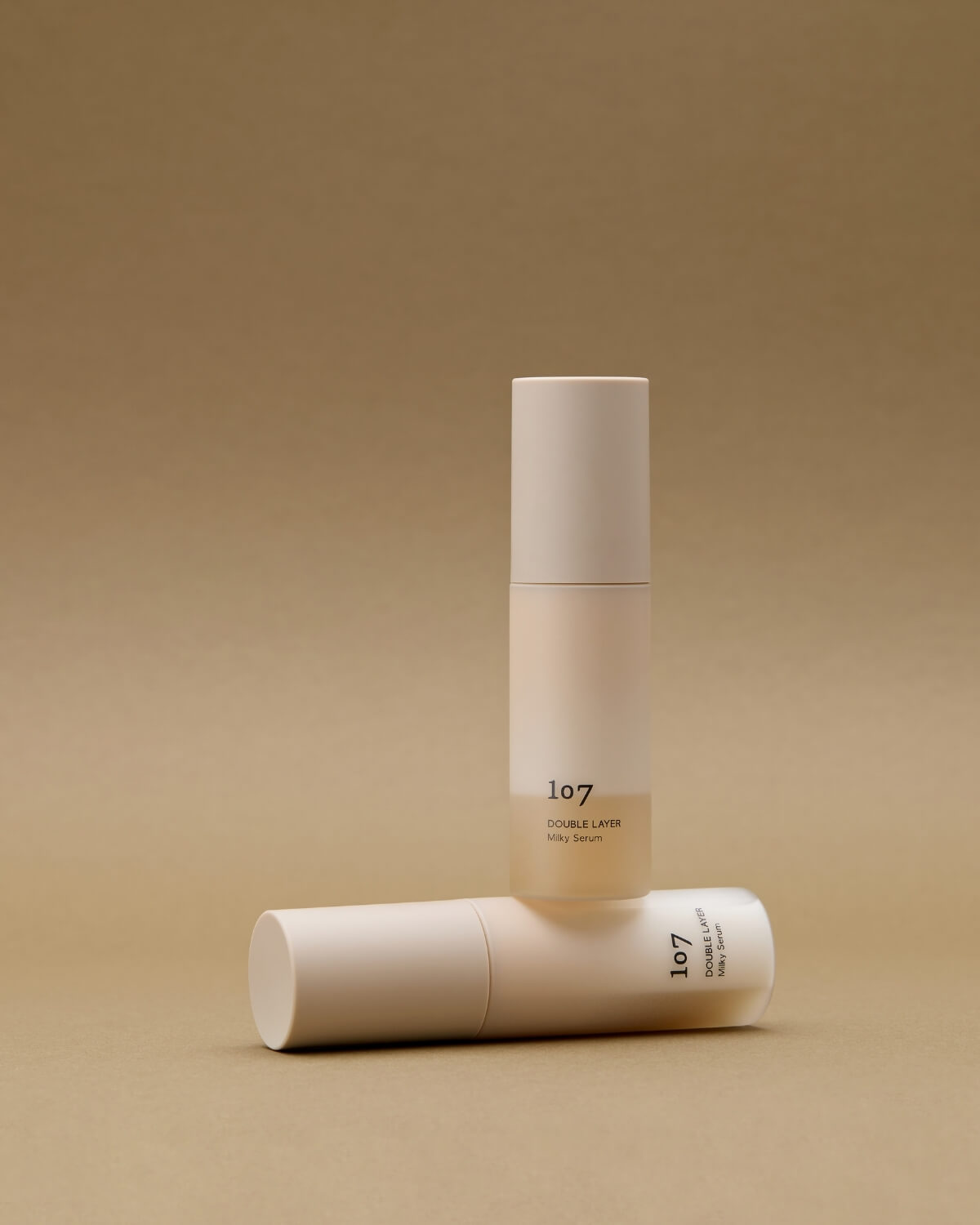 Two bottles of 107 Double Layer Milky Serum on a neutral beige background.