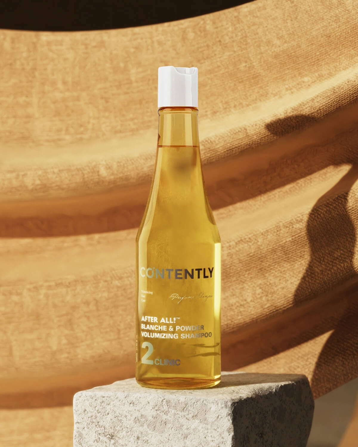 A yellow bottle of the "After All! Blanche & Powder Volumizing Shampoo" is placed on a rough, light gray stone or concrete block. The background consists of a draped, textured mustard-yellow fabric.