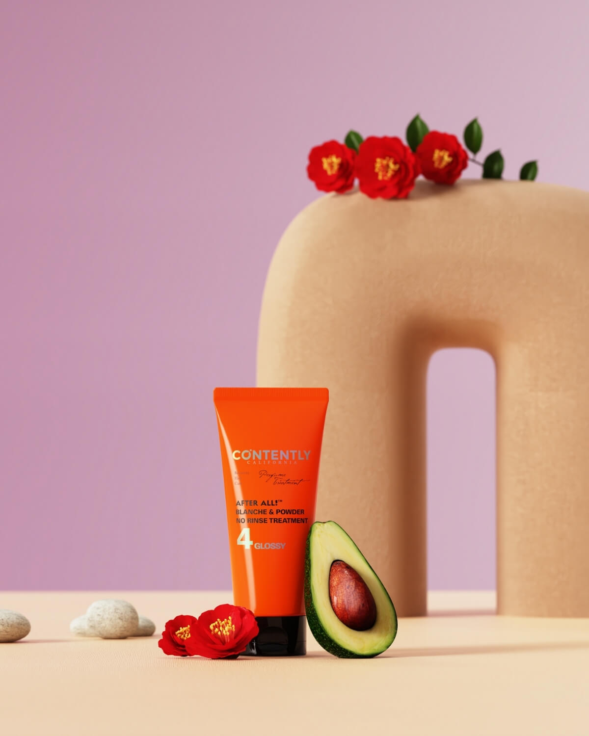 he orange hair treatment tube is placed in a still life arrangement with a halved avocado on the right, two red camellia flowers, and smooth river stones on the left. The background features a curved, beige arch object against a soft lilac wall.