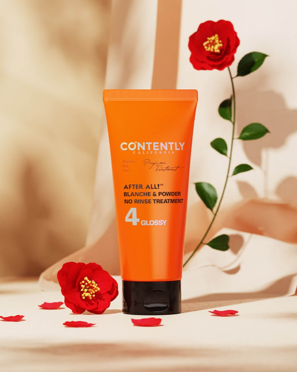 An orange tube of the hair treatment is displayed with red roses—one on a stem behind the product and one near the base. The setting features a draped, textured beige fabric backdrop and a beige surface.