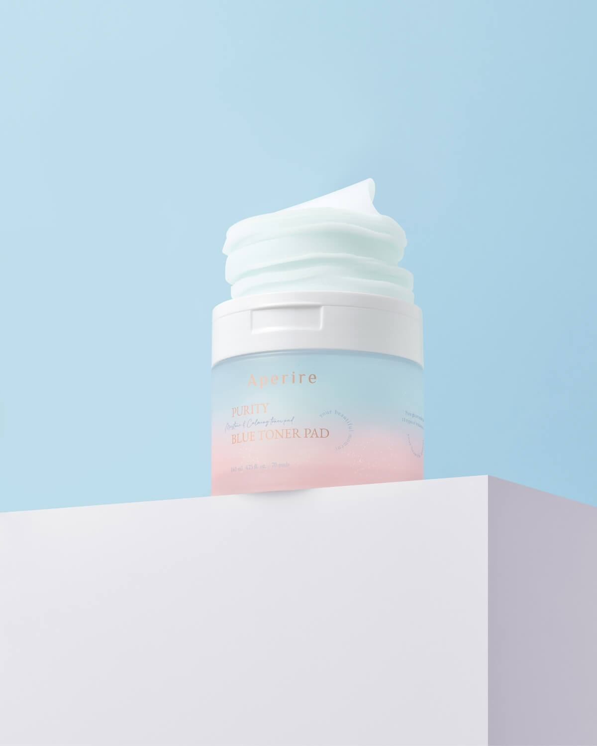 The open container of blue toner pads, with a fluffy stack of pads protruding from the top, is angled on a white pedestal against a light blue background.