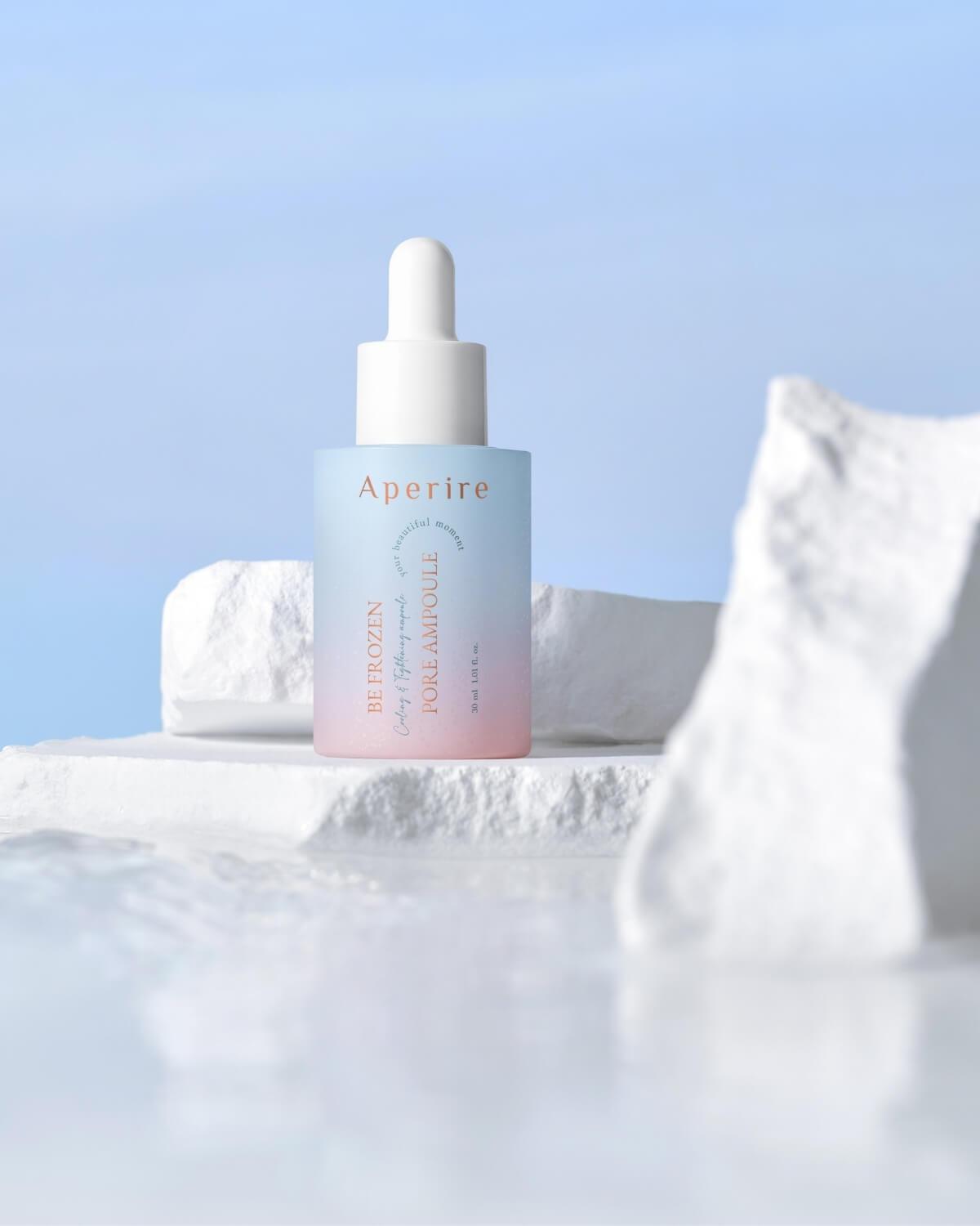 The ombre ampoule bottle with its white cap is featured on a broken white block or pedestal, set against a bright blue sky, creating a cooling, architectural product display.