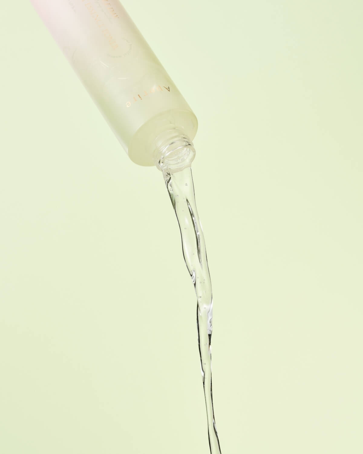 A macro close-up of a hand gently pressing a white cotton pad soaked with the amber-colored toner liquid onto the skin of a forearm.