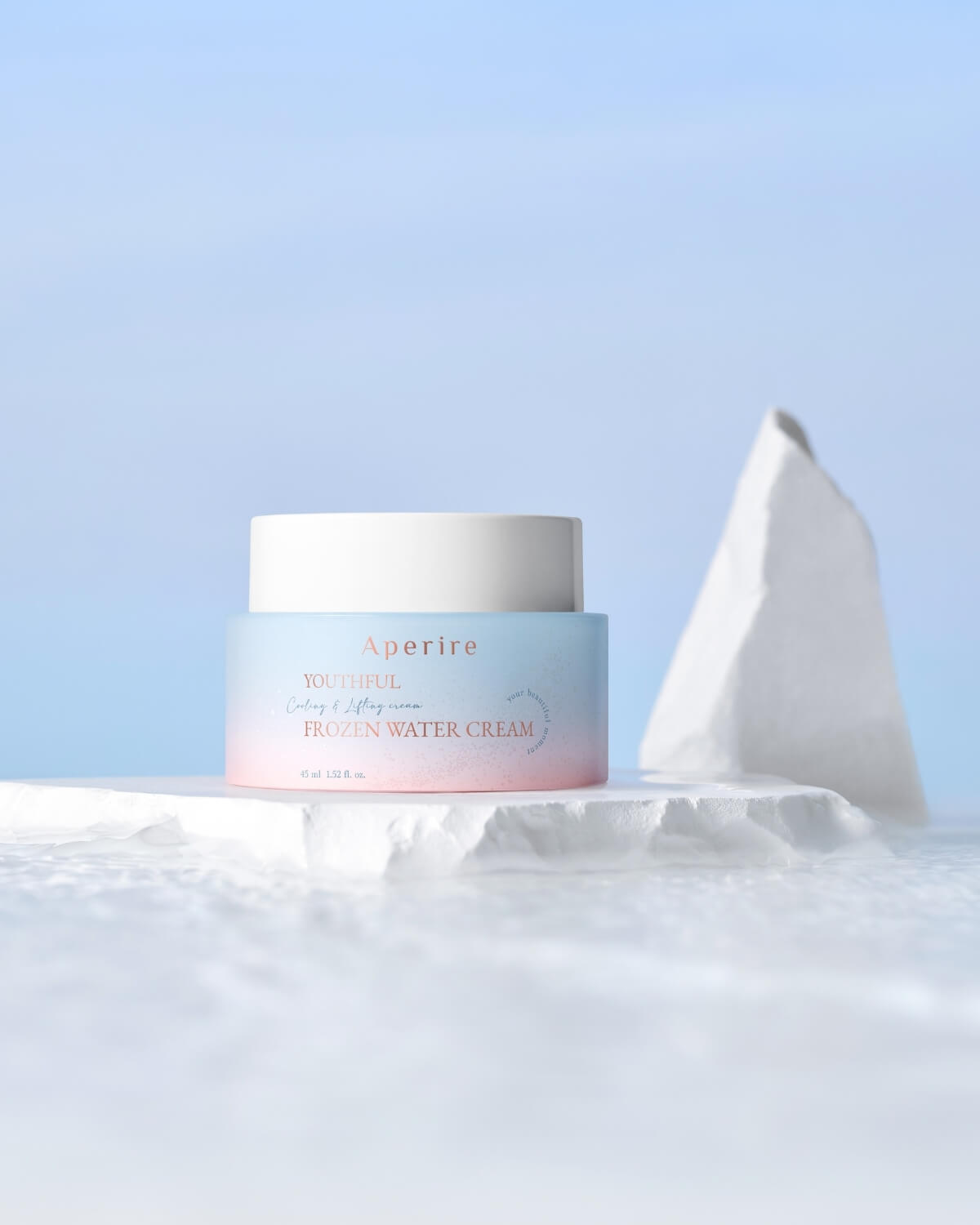 The cream jar is positioned on a cracked white block, surrounded by a subtle snowy texture, with a large, triangular white rock behind it. The background is a bright, clear blue, emphasizing the "frozen" theme.