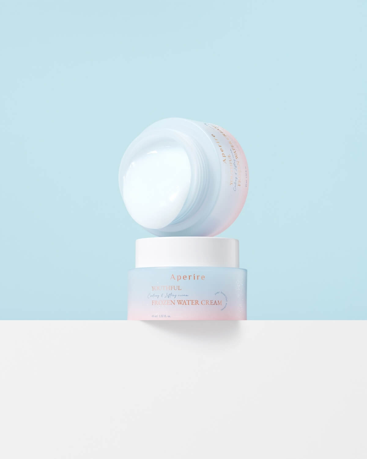 Two cream jars are stacked against a blue background: the base jar is capped and upright, while the top jar is uncapped and upside down, displaying the white cream product inside.