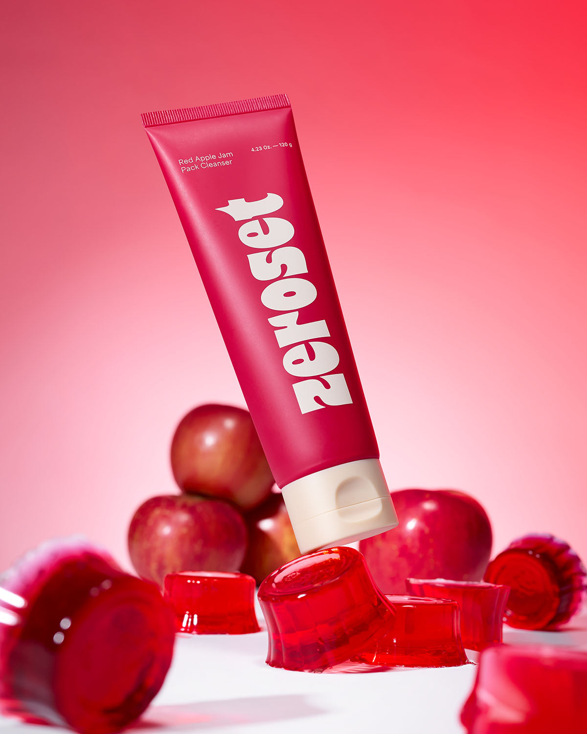 Angled view of Zeroset Red Apple Jam Pack Cleanser tube surrounded by whole apples and red jelly blocks.