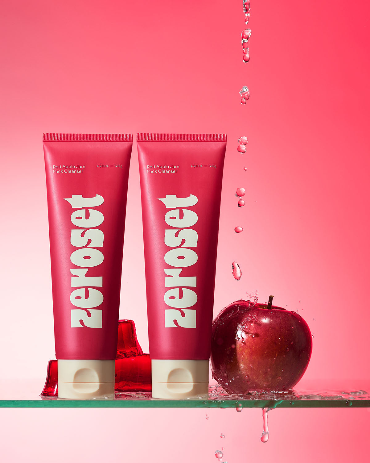 Two tubes of Zeroset Red Apple Jam Pack Cleanser on glass with splashing water, red apple, and jellies.