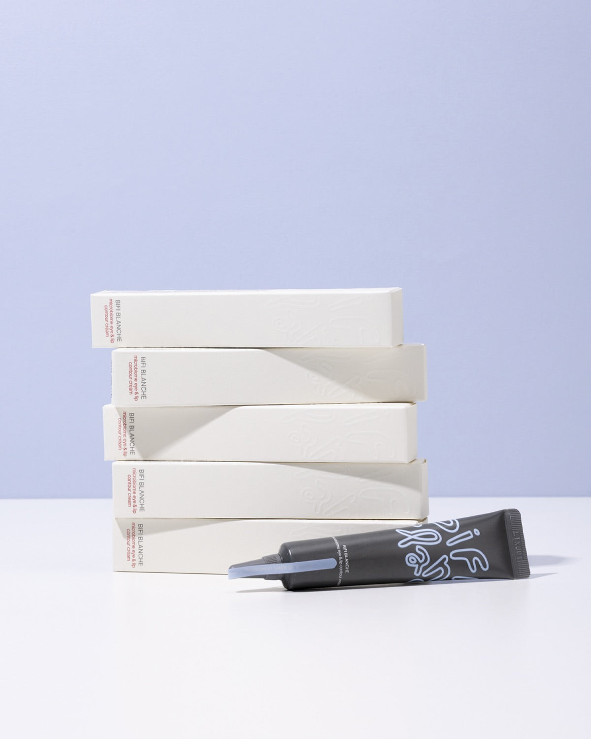 A tube of Bifi Blanche Microbiome Eye and Lip Cream lying in front of a stack of five white product boxes.