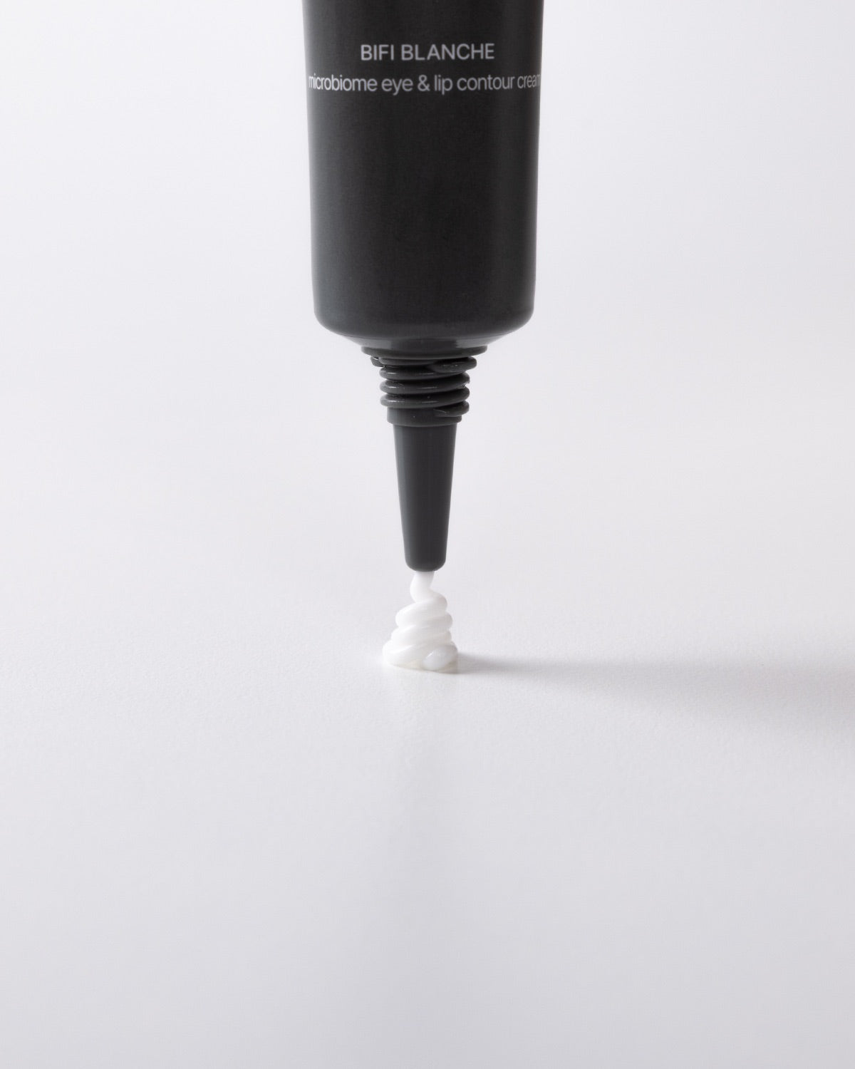 Close-up of a dark gray tube dispensing a small, coiled swirl of white skincare cream onto a white surface.