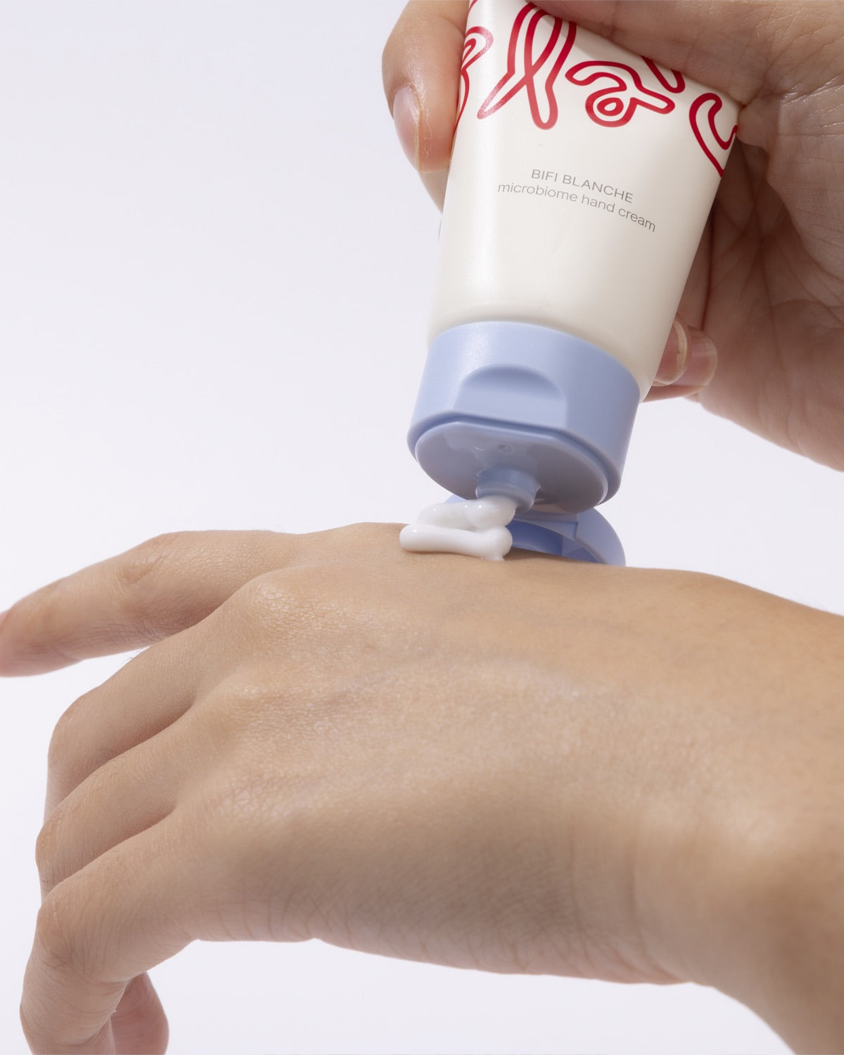 Squeezing a dollop of white Bifi Blanche Microbiome Hand Cream from the tube directly onto the back of a hand.