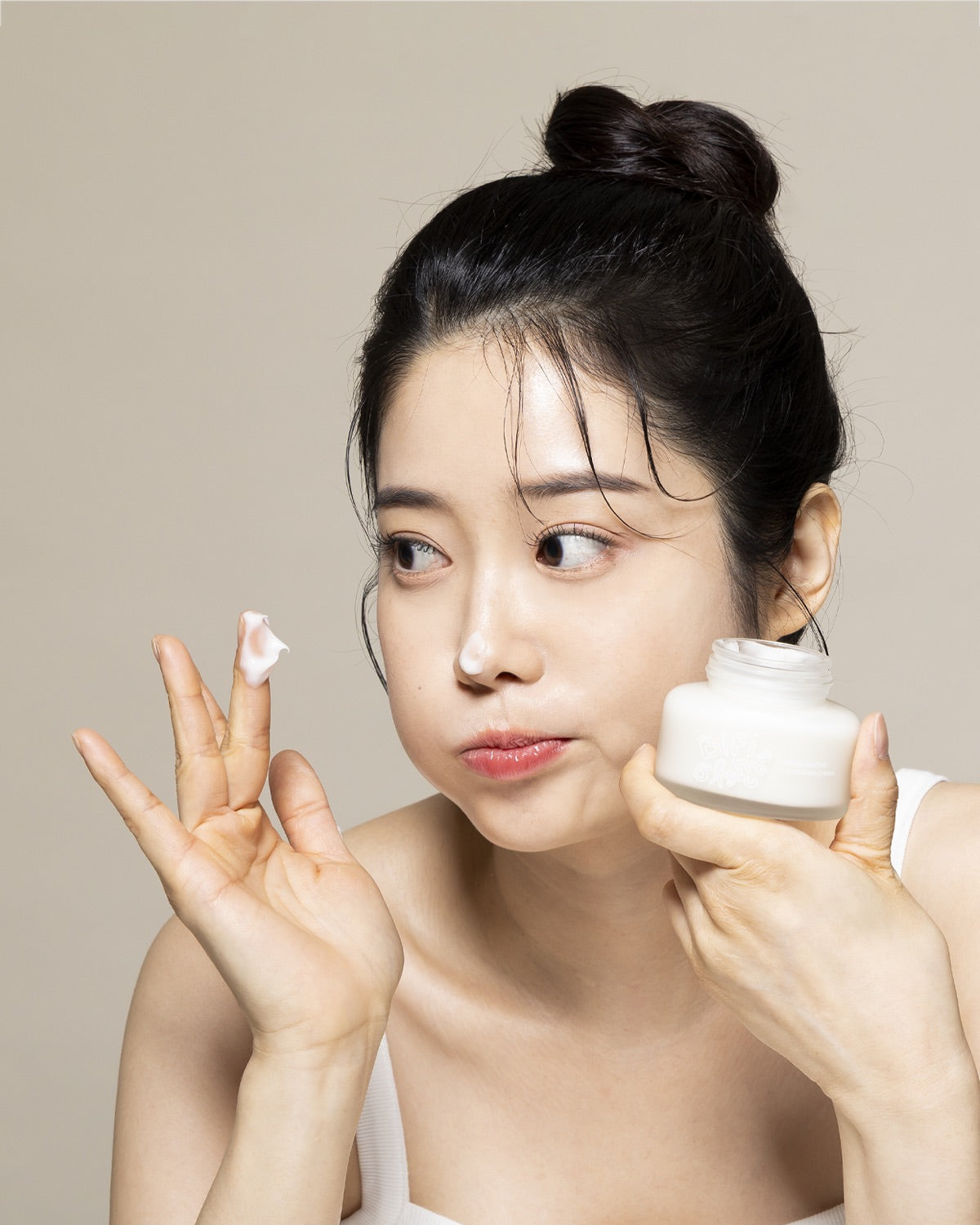 A woman holding a jar of Bifi Blanche Microbiome Moisture Cream with a dollop of cream on her finger.