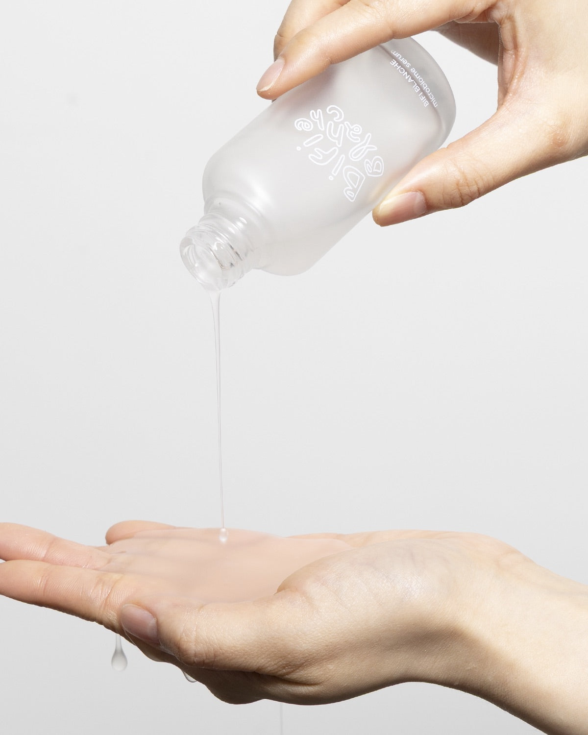 Hand pouring clear Bifi Blanche Microbiome Serum from the frosted glass bottle into an open palm.