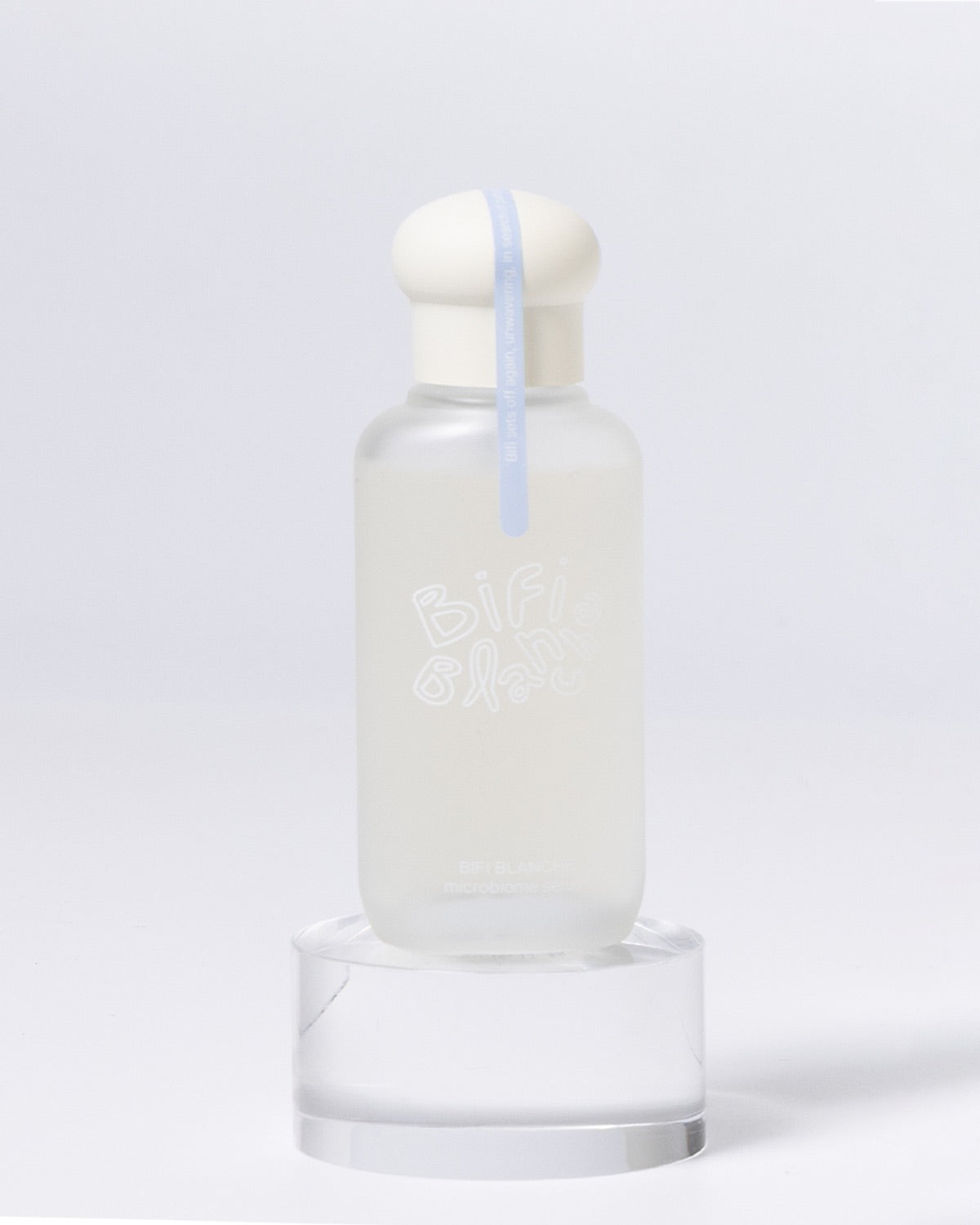 Bifi Blanche Microbiome Serum bottle displayed on a clear, round acrylic block pedestal.
