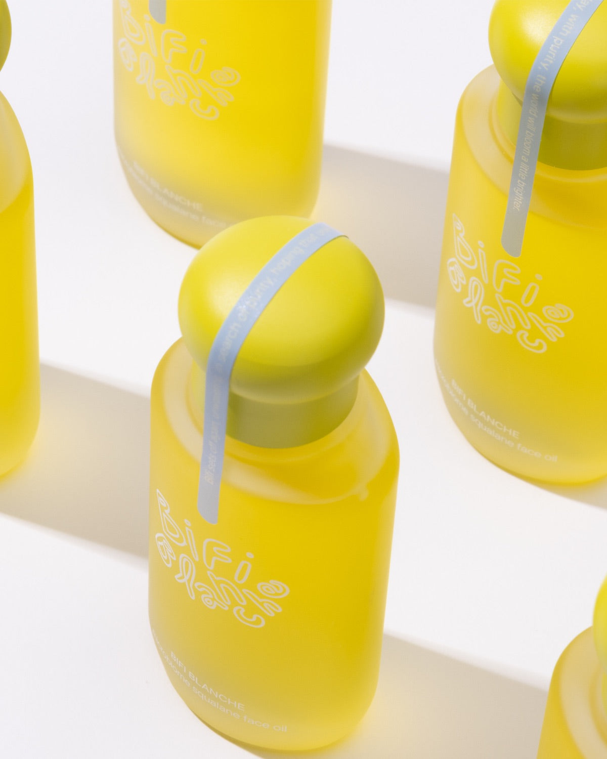 High-angle geometric arrangement of multiple yellow Bifi Blanche Microbiome Squalane Face Oil bottles.